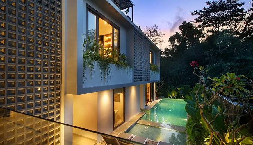 Modern villa pool area at sunset with sleek architecture, illuminated water, and lush tropical jungle surroundings at Leceni Villa