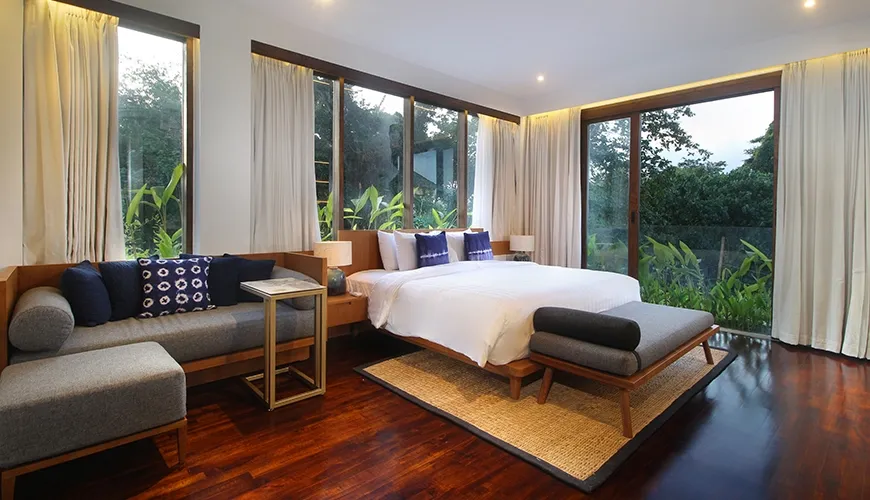 Stylish villa bedroom featuring dark wooden floors, full-height windows, and a comfortable daybed with blue cushions at Leceni Villa