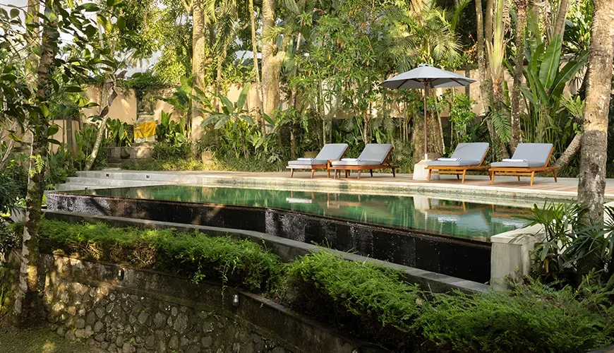 Lush green garden with swimming pool and lounge chairs at Leona Suweta