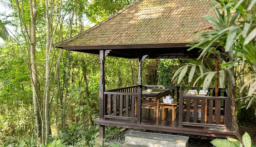 Secluded wooden spa gazebo housing massage table include amidst beautiful verdant surroundings at Leona Suweta