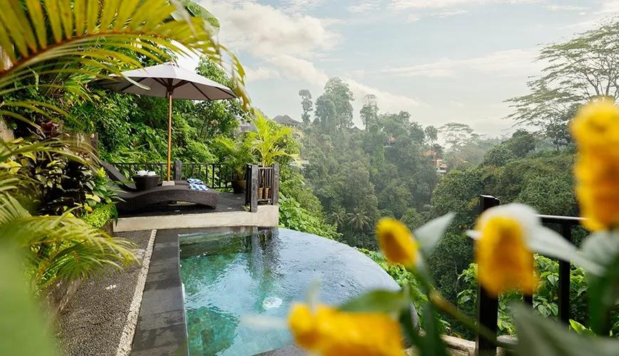 Private infinity pool with an umbrella and lounge chairs overlooks a lush jungle valley at Leona Valley View 1BR