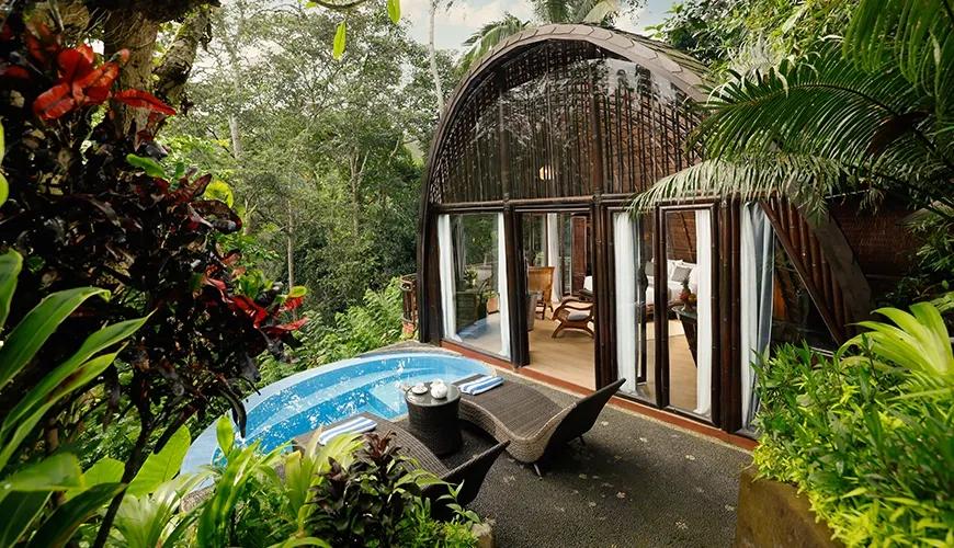 Serene pool area with lounge chairs is surrounded by lush tropical plants and a unique bamboo villa at Leona Valley View 1BR