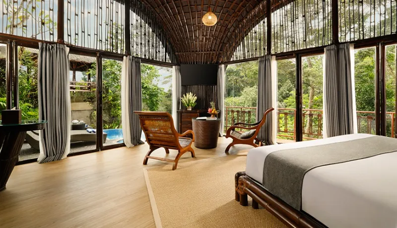 Stunning bamboo master bedroom features a bed and seating area with large windows overlooking the jungle at Leona Valley View 1BR
