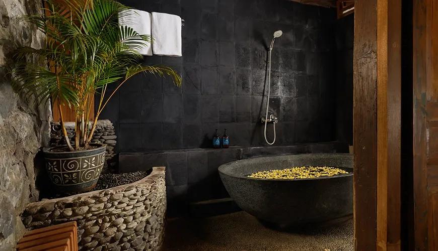 Stunning bathroom features a large stone bathtub filled with yellow flowers and a tropical plant at Leona Valley View 1BR