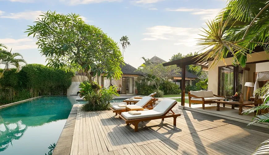 Beautiful private swimming pool with a spacious wooden deck and comfortable lounge chairs in a lush tropical garden at Nelayan Villa