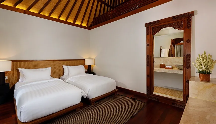 Comfortable villa twin bedroom featuring two single beds and a beautiful carved wooden doorway at Nelayan Villa