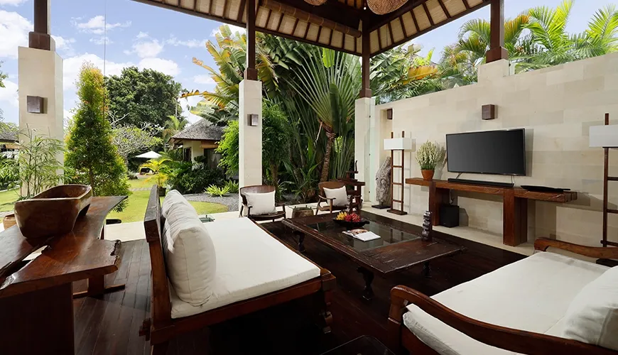 Luxurious open-air living space in a tropical villa featuring comfortable white sofas and wooden furniture at Nelayan Villa