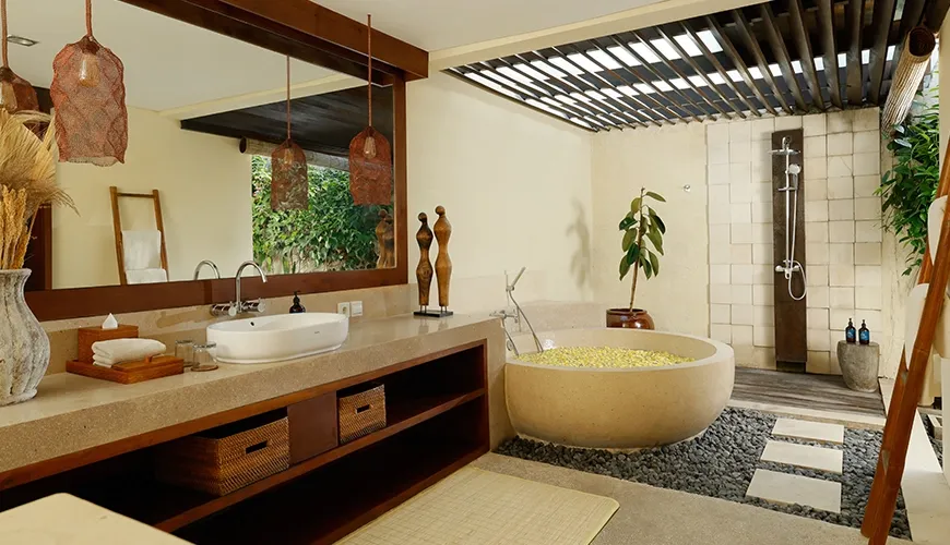 Luxurious open-air villa bathroom with a unique stone bathtub and a beautiful shower area with natural stone floors at Nelayan Villa