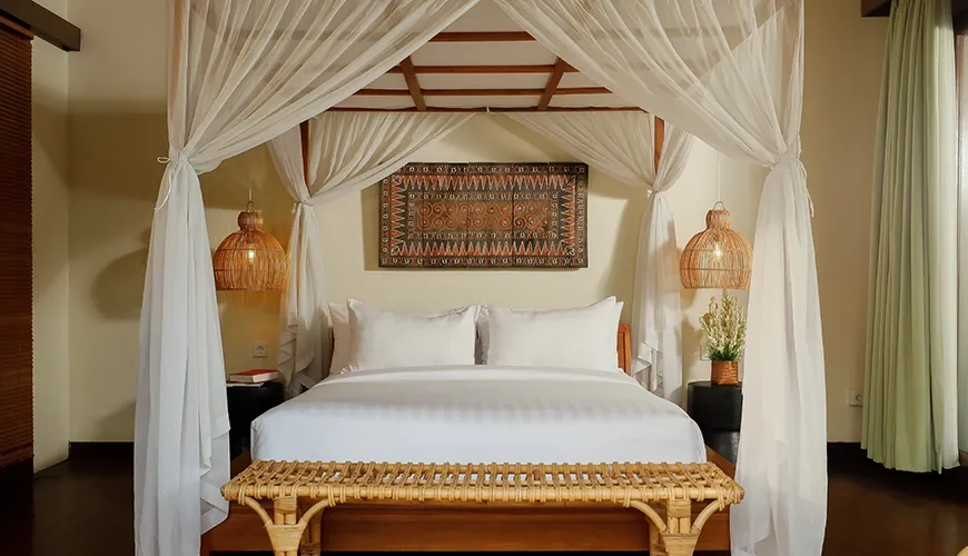 Luxurious villa bedroom featuring a romantic four-poster bed with white drapes and natural woven accents at Nelayan Villa