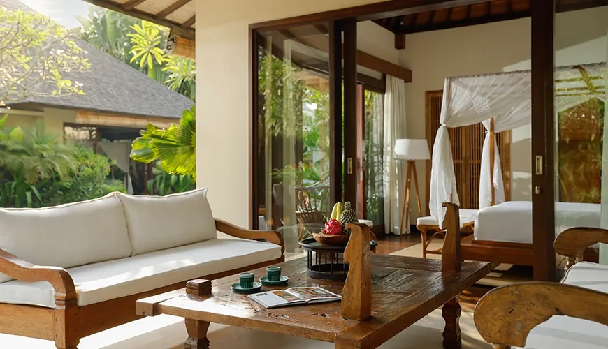 Relaxing villa terrace with comfortable wooden lounge furniture and a peaceful view of the lush tropical garden at Nelayan Villa