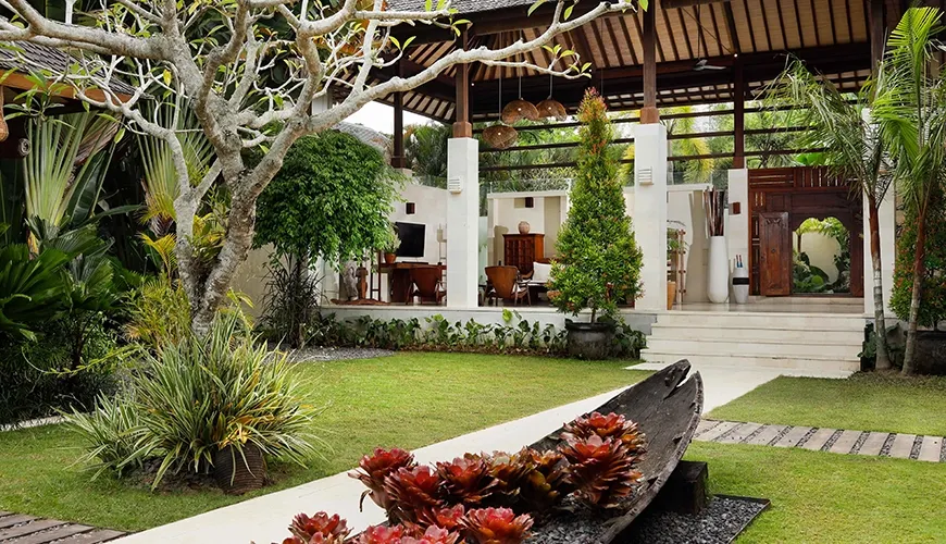Serene tropical villa garden with lush foliage, a manicured lawn, and natural stone pathways at Nelayan Villa
