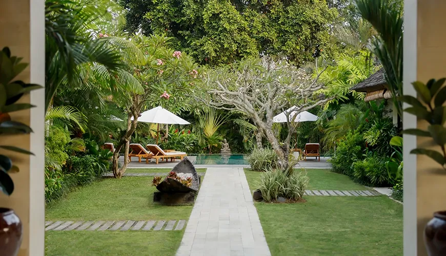Serene villa garden oasis featuring lush tropical plants, vibrant flowers, and a private, tranquil seating area at Nelayan Villa