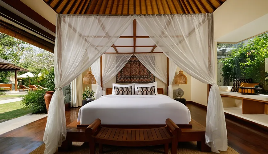 Spacious villa bedroom featuring a romantic canopy bed with elegant white drapes and natural wood furniture at Nelayan Villa