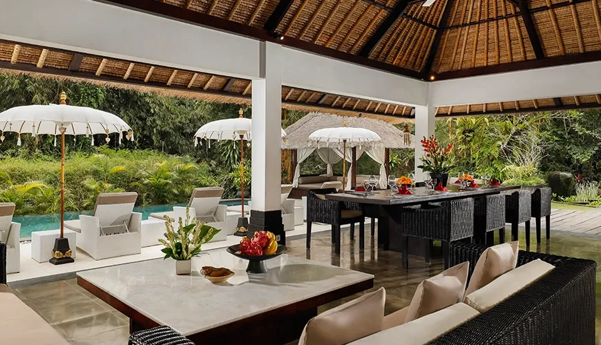 Open-air dining features thatched roof, a long table, and pool view at Omecure