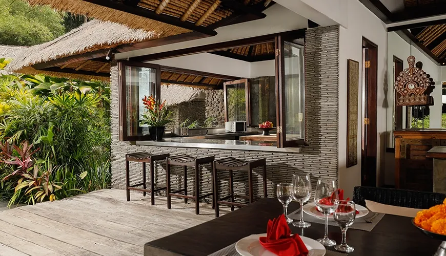 Outdoor kitchen features a bar counter and vibrant tropical plant views at Omecure