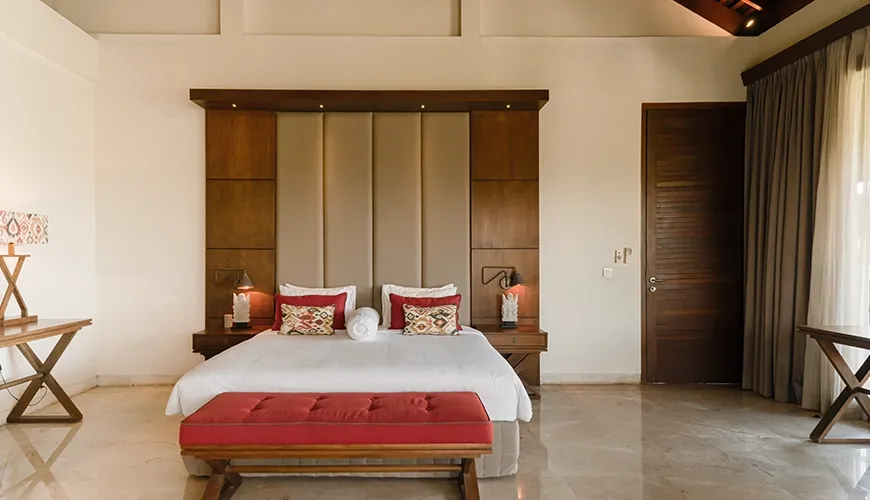 Elegant villa bedroom with a large wooden headboard, a vibrant red bench, and polished marble flooring for a luxury guest stay at Omekai Cemagi