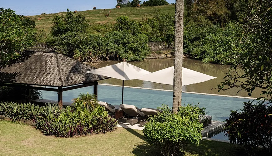 Lush villa garden area next to the infinity pool, featuring sun loungers, resort umbrellas, and a shaded traditional gazebo at Omekai Cemagi
