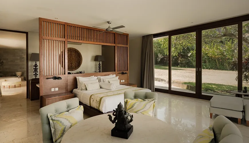 Spacious master bedroom featuring a stunning wooden headboard, a cozy sitting area, and large glass doors opening to the villa garden at Omekai Cemagi