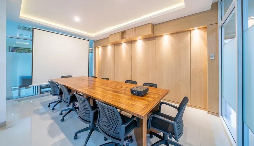 Modern meeting room wooden table black chairs projector screen light wood walls at Sara Residence