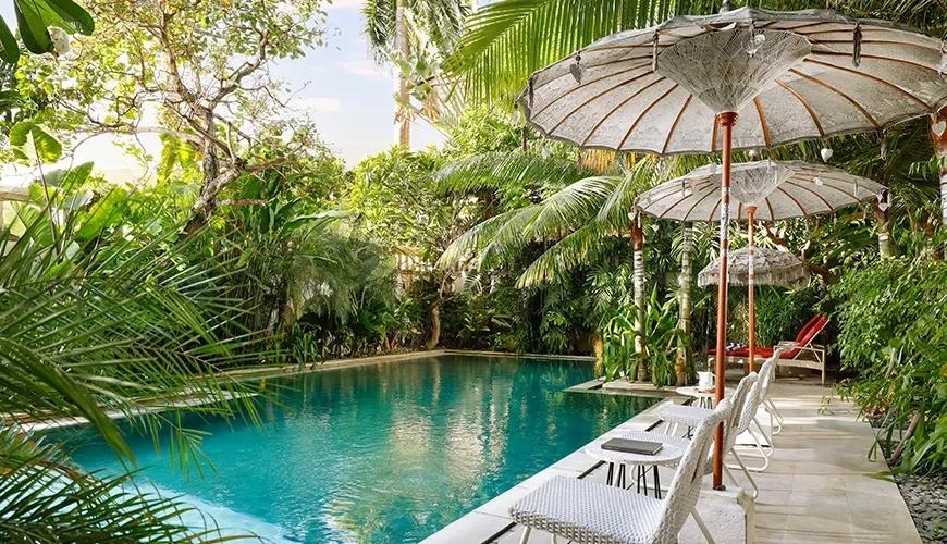 Serene swimming pool white lounge chairs traditional parasols lush tropical garden at Sara Residence