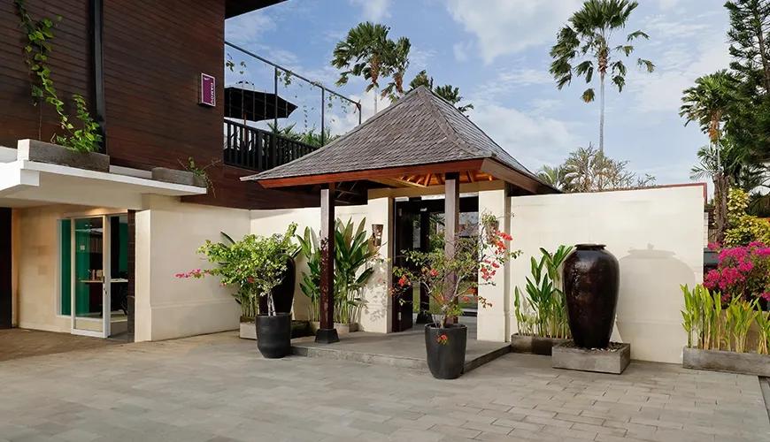 Elegant villa entrance with a traditional wooden roof, lush tropical greenery, and a welcoming pathway leading inside at Shanti Estate 1BR