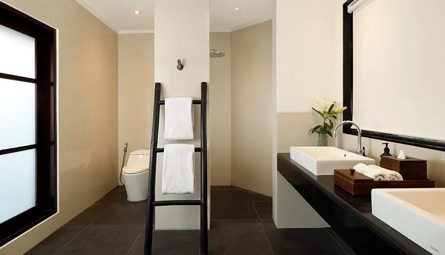 Minimalist Japanese inspired bathroom featuring dark stone tiles with a black bamboo towel ladder rack at Shanti Estate