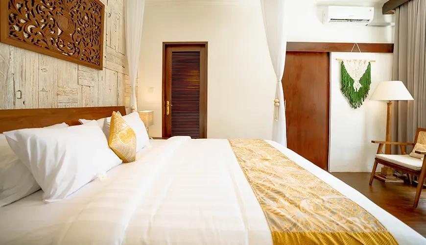 Modern tropical bedroom with wooden accents, white bedding, and gold pillows at shanti estate
