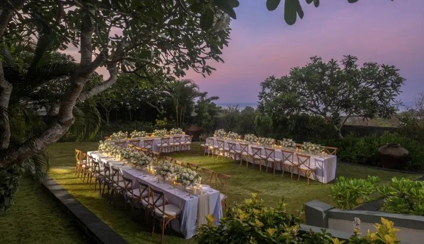 Beautiful outdoor wedding reception setup with long tables and floral arrangements under a vibrant sunset sky at Shanti Residence