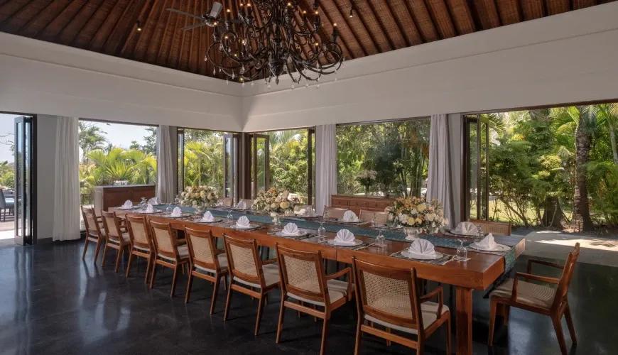Elegant villa dining featuring a long wooden table and ornate chandelier with lush tropical garden views at Shanti Residence
