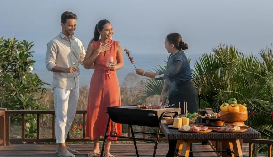 Friendly villa chef serving fresh grilled skewers to a happy couple during an outdoor barbecue party at Shanti Residence