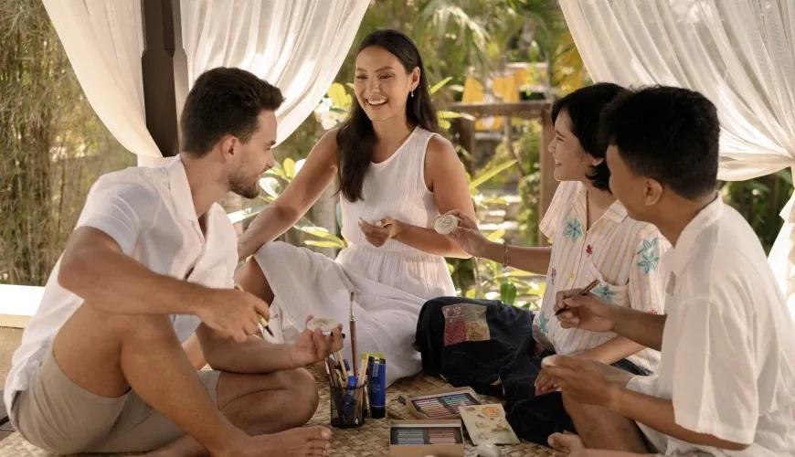 Happy group of guests enjoying a creative stone drawing activity in a breezy tropical villa gazebo at Shanti Residence