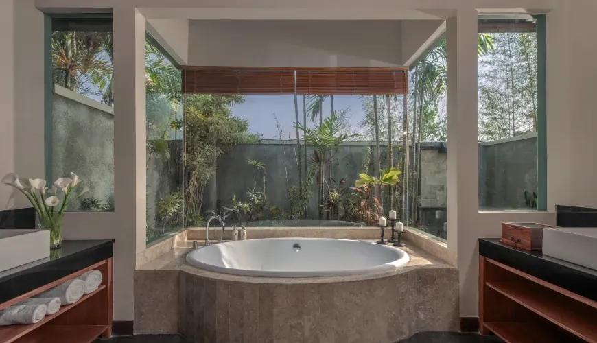 Luxurious bathroom featuring a large circular soaking tub surrounded by glass windows overlooking a tropical garden at Shanti Residence