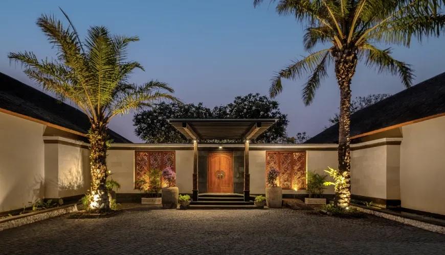 Luxurious tropical villa entrance featuring large palm trees and warm sunset lighting on a cobblestone driveway at Shanti Residence