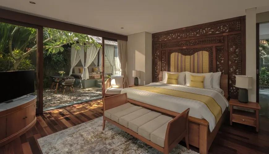 Luxurious villa bedroom with an ornate wooden headboard and sliding doors opening to a private tropical garden at Shanti Residence