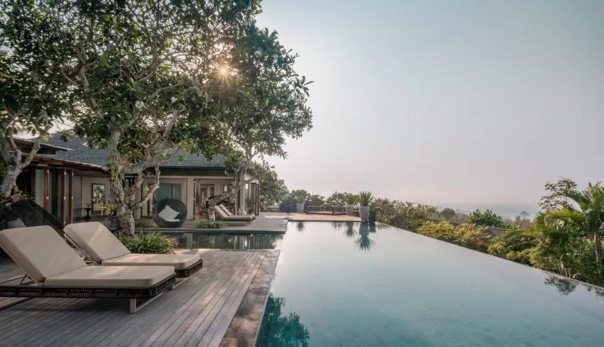 Modern infinity pool at a luxury villa overlooking the ocean with comfortable sun loungers and greenery at Shanti Residence
