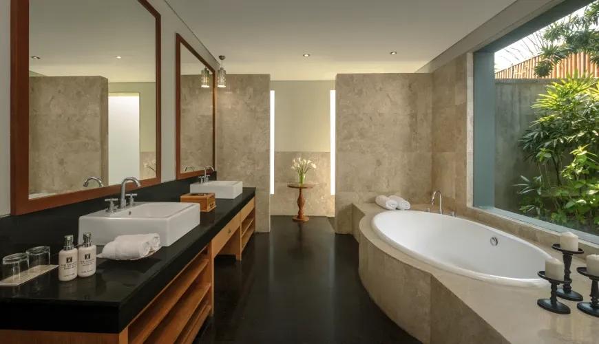 Modern villa bathroom featuring double sinks and a large soaking tub next to a lush tropical garden view at Shanti Residence