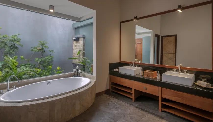 Modern villa bathroom with double vanity sinks and a large soaking tub beside a lush private garden at Shanti Residence