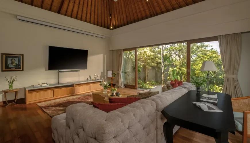 Modern villa entertainment room featuring a large television and comfortable tufted sofa with a lush garden view at Shanti Residence