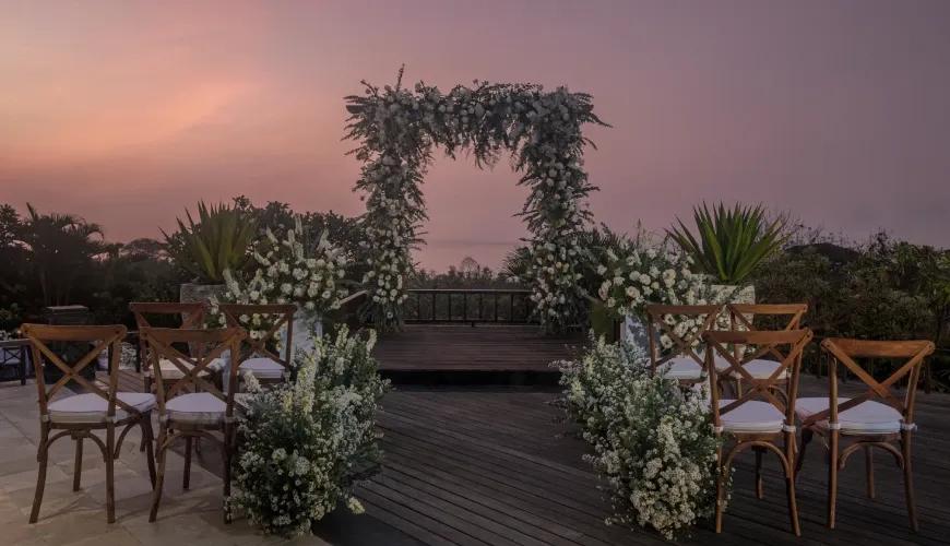 Stunning outdoor wedding chapel with white floral arrangements on a wooden deck at sunset at Shanti Residence