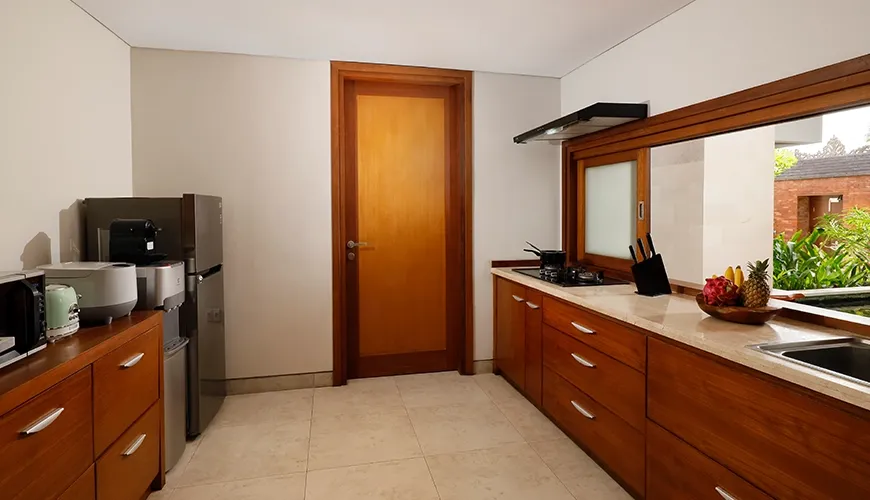 Modern kitchen with wooden cabinetry, stainless steel appliances, and a window overlooking greenery at The Bija