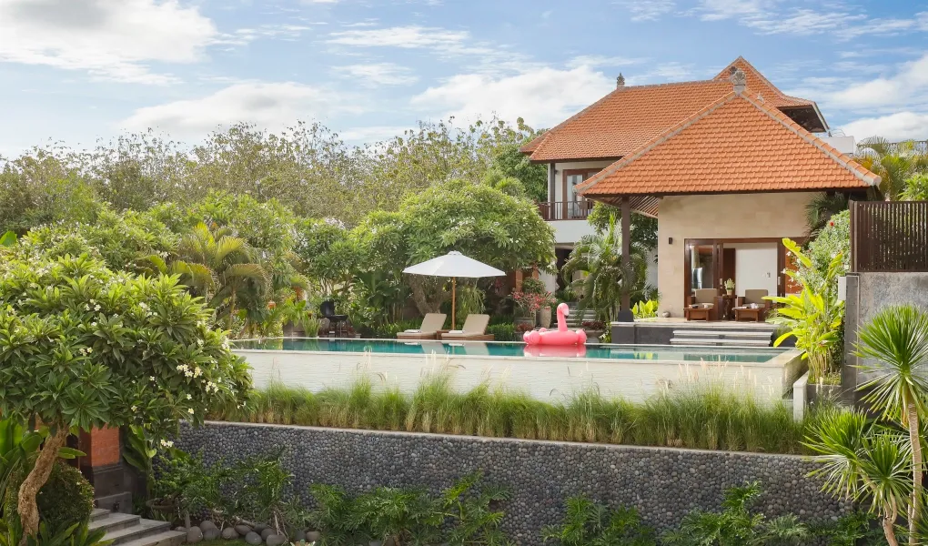 Private villa pool surrounded by lush greenery and a stone wall at The Bija Villas