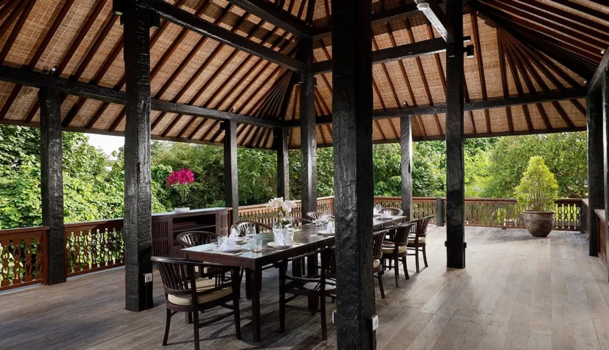 Traditional Balinese Joglo pavilion with a long dining table, dark wood, and lush green views at The Bija Villas