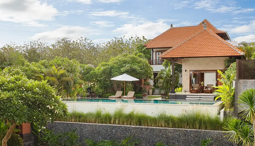 Traditional Balinese villa with a large outdoor pool, sun loungers, and lush tropical trees at The Bija Villas