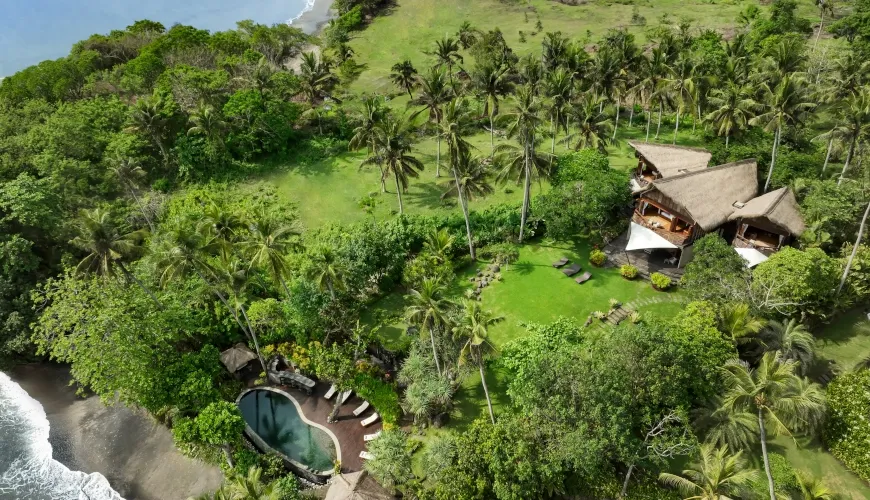 Aerial view of luxury Balinese villa, surrounded by tropical foliage, near a black sand beach at The Cove Bali