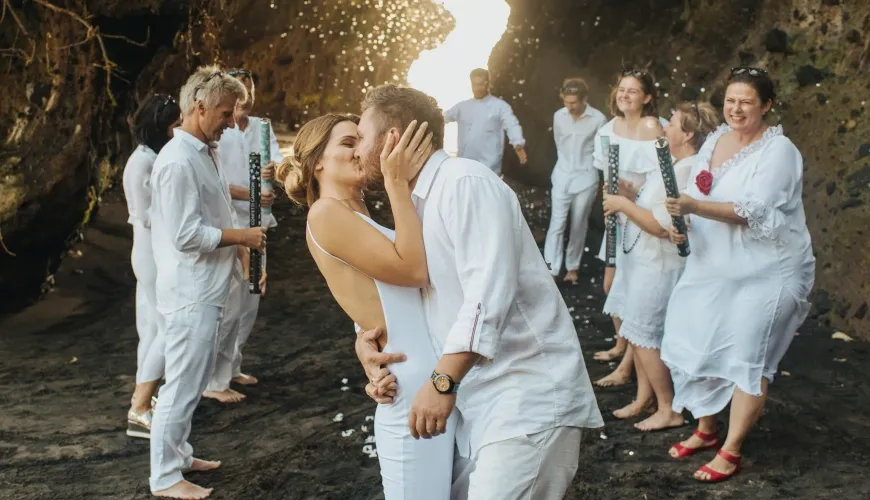 Happy couple kissing at beach wedding ceremony surrounded by loved ones at The Cove Bali