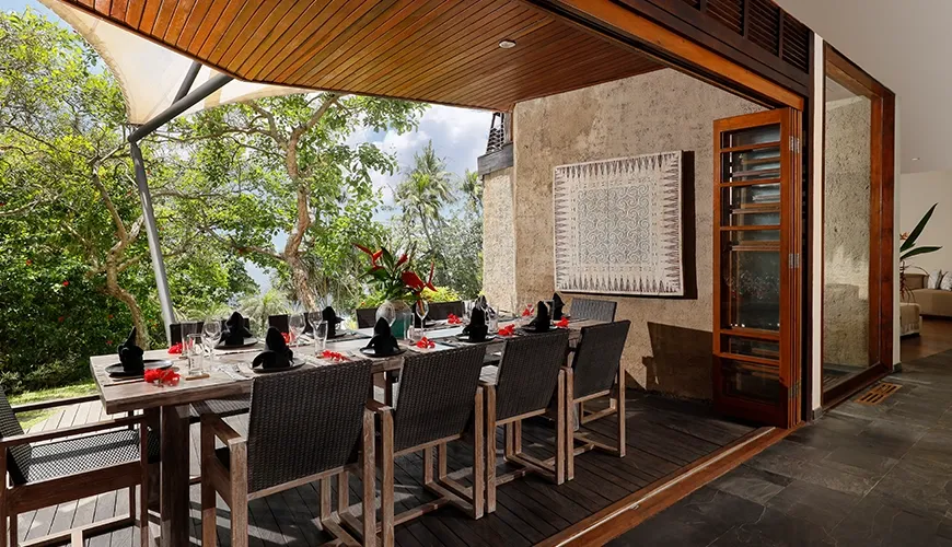 Outdoor dining features a long table with lush tropical ocean backdrop at The Cove Bali