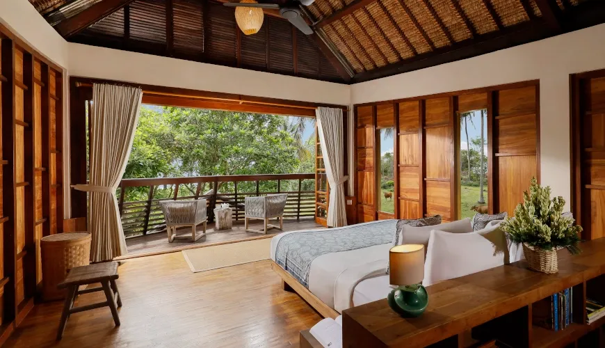 Rustic wooden bedroom with thatched roof and balcony overlooking tropical garden at The Cove Bali