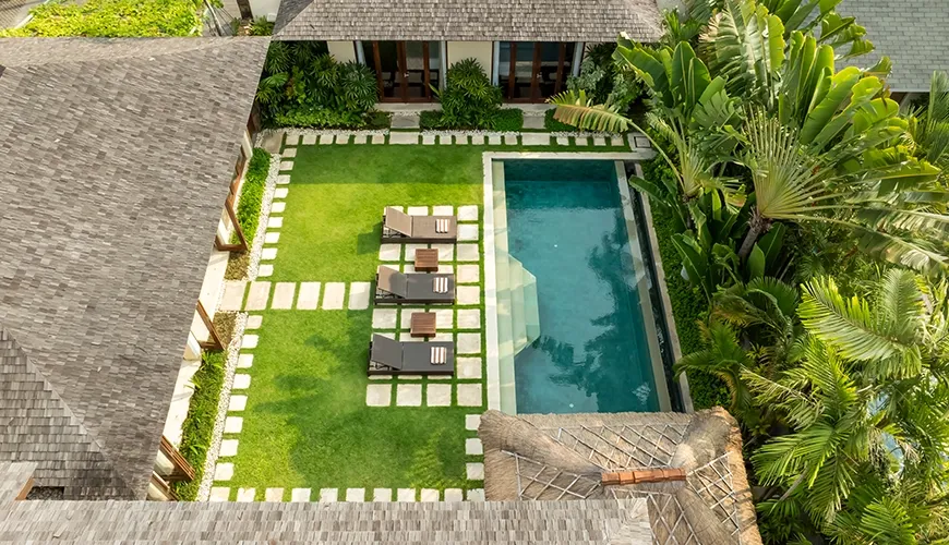 Aerial view of a stunning tropical villa pool with a spacious lawn and lounge chairs at The Suar Seminyak