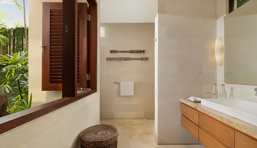 Beautifully designed bathroom with natural wood accents and an open window with lush tropical plants at The Suar Seminyak