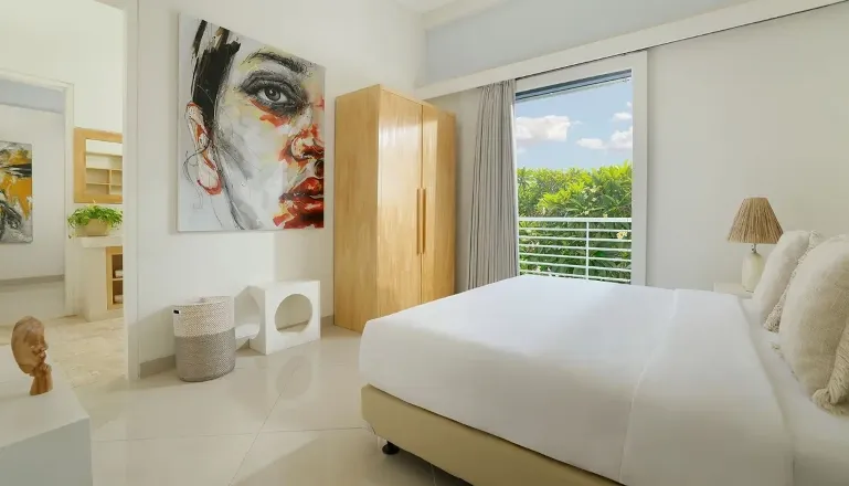 Cozy bedroom with a large bed, modern abstract art, and a wooden wardrobe at The Suar Sanur
